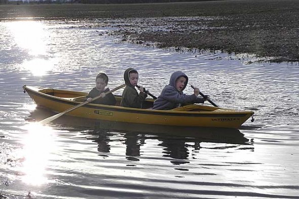 From left, Will, Noah and Logan Spracklen canoed across a flooded farm field earlier this week at the family’s Green Township home, where in a normal year the corn would already be several inches high. (Submitted photo)