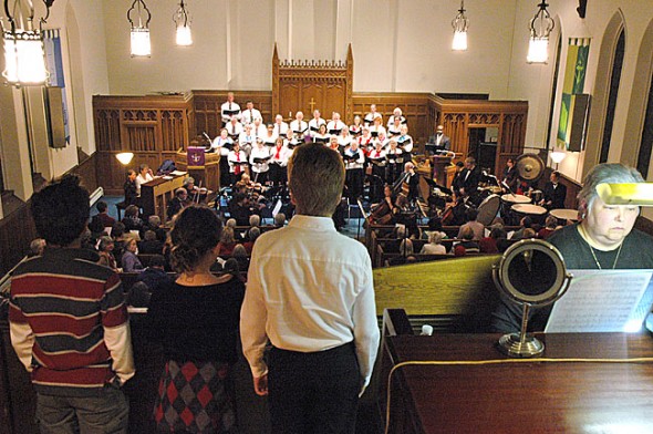 The Yellow Springs Community Chorus and Chamber Orchestra presented a grand holiday musical spectacle with the performance of Benjamin Britten’s “St. Nicolas,” featuring tenor Vincent Davis, at the First Presbyterian Church Sunday, Dec. 18. Overlooking the ensemble from the choir loft was the trio singing the part of the “pickled boys” — three children said to have been brought back to life by the saint — from left, David Walker, Eliza Minde-Berman and Danny Grote; organist Susanne Grote is at right. (Photo by Matt Minde)