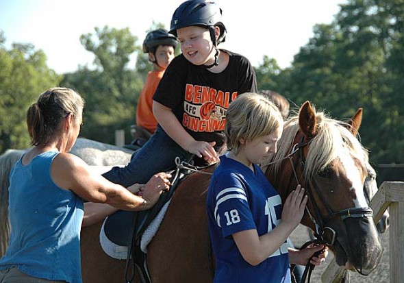 Evan Martin, a participant in the Riding Centre’s therapeutic riding program, mounted Apollo last Saturday, with the help of local high school volunteer Anna Mullin and Riding Center manager Carolyn Bailey. Mullin and a small group of other local girls provide one-on-one help for the riders, most of whom have mental and physical disabilities and would be less safe riding without assistance. The therapeutic riding program would not be possible without the dozens of volunteers who have supported it since it began in 1974. (Photo by Lauren Heaton)