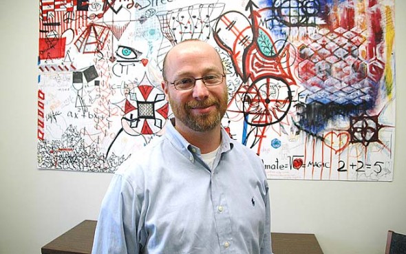 This month Dan Doron, of Columbus, joined Antioch College as its new director of communications. Doron has worked at several newspapers, the PR department of the Cleveland Clinic and Yale University, and he hopes to improve communication with the local community and the college’s neighbors. Here Doron stands before a piece of student artwork he found to adorn his walls. (Photo by Megan Bachman)