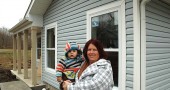 New first-time homebuyer Julie McCowan, holding her grandson, Dylann, in front of the Cemetery Street home she recently purchased through Home, Inc. for her four-person family (plus frequent visits from “little ones” like Dylann, she said). Villagers wishing to celebrate with McCowan and her family and learn more about Home, Inc.’s Cemetery Street development are invited to an open house at 138 Cemetery St. on Friday, Jan. 29, from 5 to 7 p.m. (Photo by Audrey Hackett)