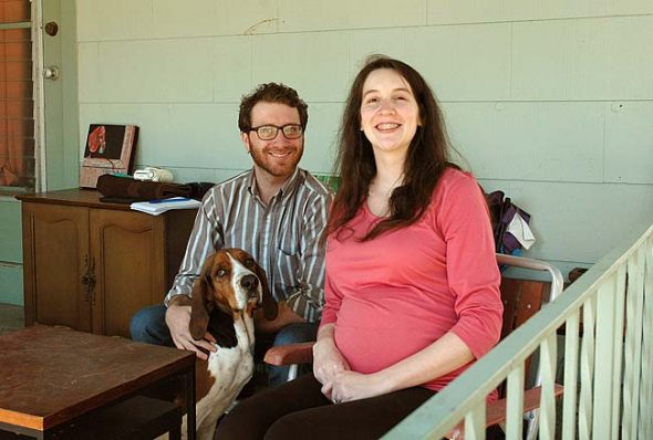 Cory and Amanda Howard, with Townes, a Walker Coonhound they rescued, enjoyed a recent sunny Saturday afternoon on their Cliff Street porch. The couple moved to the village over four years ago. With a rental they love, jobs in the area and their first child on the way, the couple is putting down roots in Yellow Springs. (Photo by Audrey Hackett)