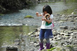 In Antioch School’s Forest Kindergarten program, the outdoors serves as laboratory and playground. Pictured, Kaede Eto took water samples from the river last month — while also holding fast to her doll. (Photo by Carol Simmons)
