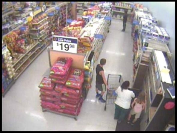 A video still showing John Crawford III, at the far end of the aisle, and shopper Angela Williams and her two children in the foreground. The still is from a Walmart surveillance video from the night of Aug. 5, 2014. (From Walmart security cameras, Youtube)