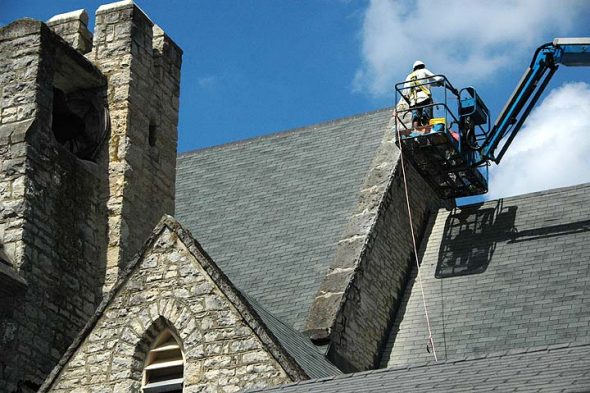 Precariously extended on a hydraulic lift, tuckpointers Roger Wood and Will Redd reset the mortar around the ancient stones at the very top of the First Presbyterian Church. The job is a dusty one, requiring the removal of old loose mortar through chipping and grinding, mostly by hand, then filling in the spaces with fresh mortar and powdered lime — at 80 feet up and 90°F temperatures. (photo by Matt Minde)
