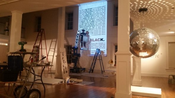 Living in Divided States exhibition installation with Michael Casselli's US/THEM mirrored disco ball in foreground, Umvikeil G. Scott Jones' "Suite for John Crawford, III" text in background being painted by Syvia Newsome. (Submitted photo)