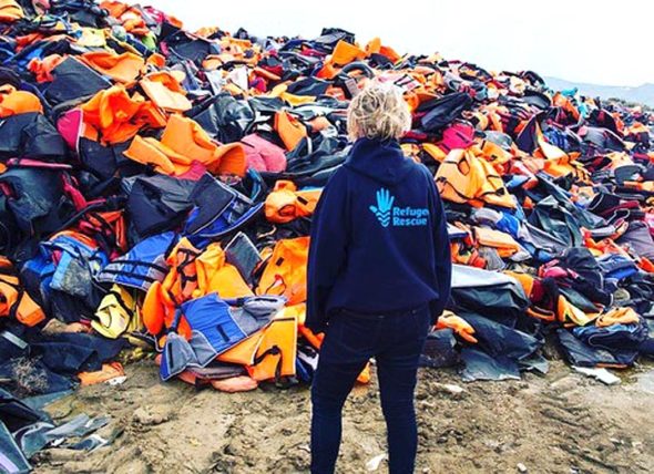 A volunteer for Refugee Rescue on the Greek island of Lesbos, which meets boats full of refugees as they arrive, is shown in front of a huge pile of life jackets used by refugees fleeing their homelands. Villager Regina Brecha, along with Anna Williamson, also of Yellow Springs, are currently among the volunteers. Her mother, Kaethi Seidl, and Beth Holyoke, who have both volunteered at Greek refugee camps, are holding a fundraiser for the cause on Tuesday, Dec. 5, at 7 p.m. at the Yellow Springs Brewery. (Submitted Photo)