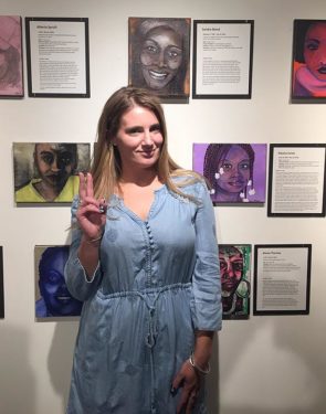 Artist Aimee Wissman stood before the paintings from her exhibit, “They Will Shoot Her Too,” a collection of portraits of women victims of police violence. The exhibit is showing at the Emporium through Aug. 1. (Submitted photo by Odette Chavez-Mayo)