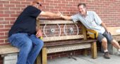A memorial bench for village resident Don Benning, who died last year, is in place in front of Tom’s Market, thanks to the efforts of lifelong family friend Shelly Blackman, left, who commissioned locally based artisan Bruce Parker, right, to create the bench that reflects Benning’s multiple interests. (photo by Carol Simmons)