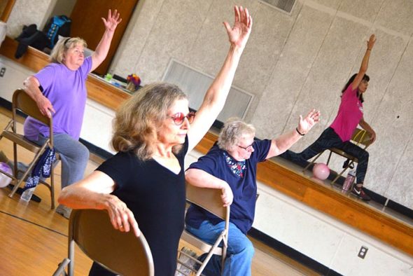 Jane Blakelock, center, stretched during a Sit Strong senior fitness class at the John Bryan Community Center this week. From the stage, fitness instructor Lynn Hardman called out and modeled the next move. Hardman, who is passionate about senior wellness, is starting a new workshop in the village focused on balance. (Photo by Megan Bachman)