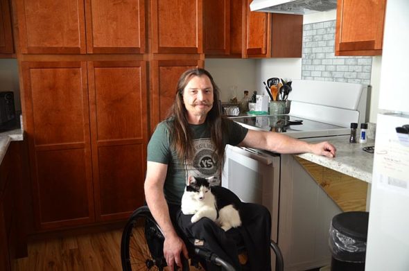 Nick Cunningham and his Japanese bobtail cat, Manny, in the fully accessible kitchen of Cunningham’s new rental apartment at 511 Dayton St. The apartment, one half of a newly built duplex, is part of Forest Village Homes, an affordable, accessible rental project developed by Home, Inc. to meet local rental housing needs. (Photo by Audrey Hackett)
