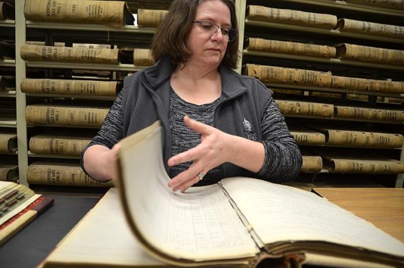 Greene County Archivist Robin Heise flips through property records detailing all the plots of land owned by Yellow Springs founding father William Mills in the 19th century. (Photo by Lauren “Chuck” Shows)
